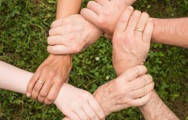 6 Hände halten sich gegenseitig am Handgelenk und bilden einen Kreis